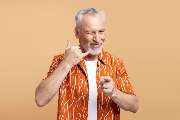 Positiver grauhaariger älterer Mann zwinkert und zeigt mit dem Finger in die Kamera, isoliert auf beigem Hintergrund. Rufen Sie mich an