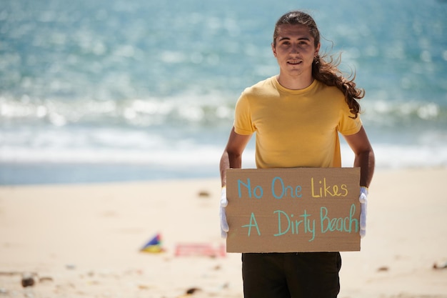 Positiver junger Aktivist, der niemand mag ein schmutziges Strandplakat hält