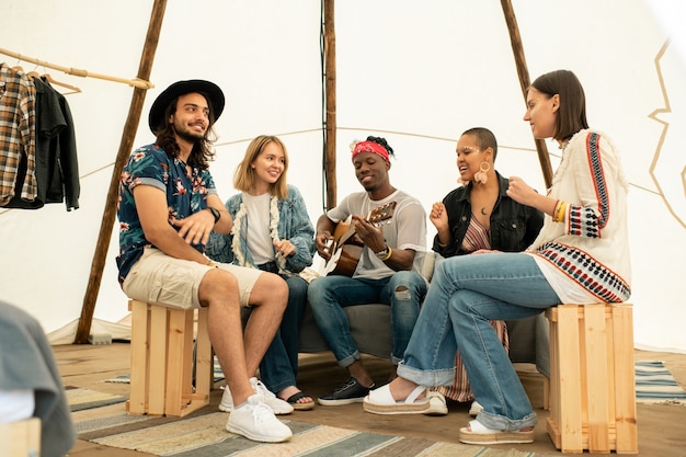 Positiver junger Musiker, der Gitarre spielt und Lied mit Freunden im Zelt singt