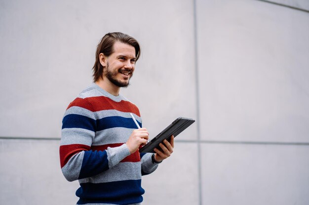 Positiver kaukasischer Freiberufler, der mit digitalem Tablet steht und online mit Geschäftspartnern chattet