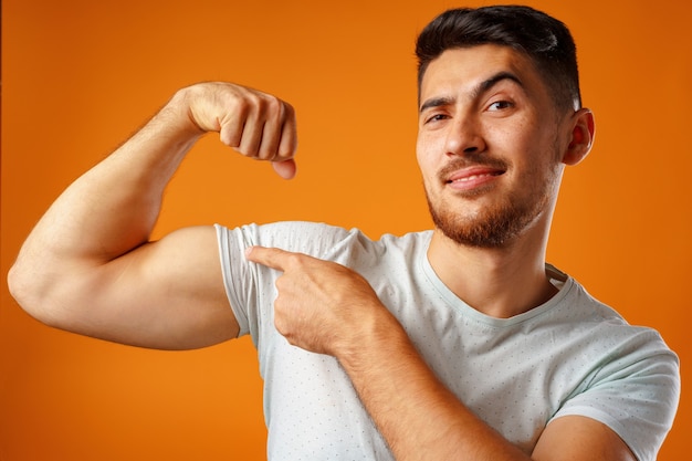 Positiver lächelnder junger Mann, der seine starken Arme gegen gelbe Oberfläche zeigt