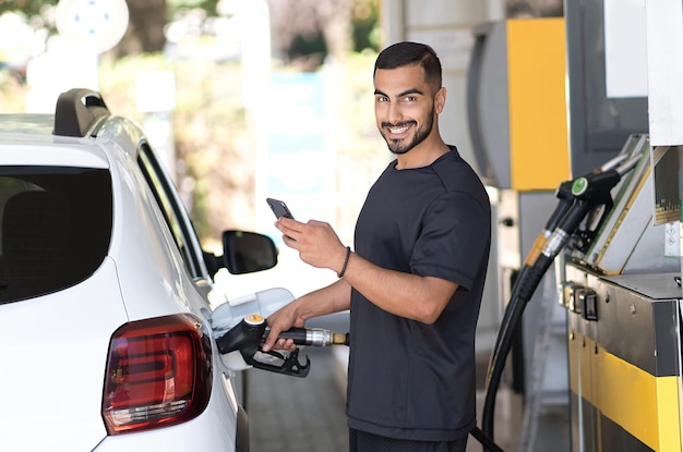 Positiver Mann, der sein Luxusauto betankt und Smartphone an der Tankstelle benachrichtigt