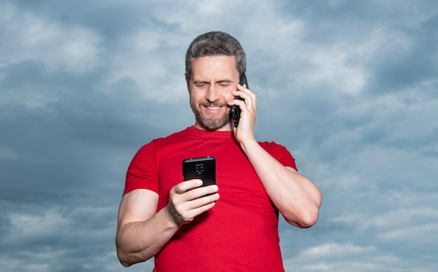 Positiver Mann hat Telefongespräch auf Himmelshintergrund Mann hat Telefongespräch im Freien