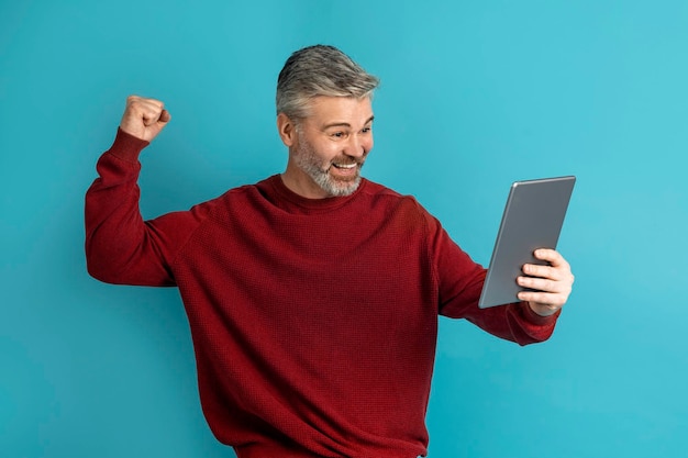 Positiver Mann mittleren Alters feiert Erfolg mit digitalem Tablet
