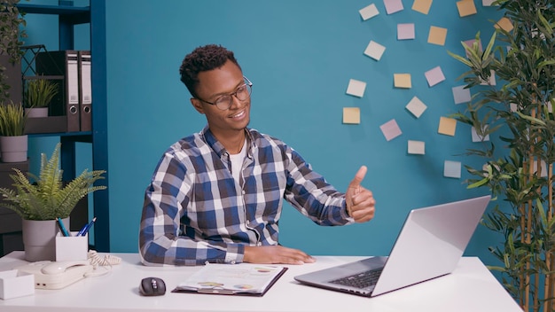 Positiver Mitarbeiter, der vor dem Laptop-Bildschirm Daumen hochgibt, Zustimmung und gutes Symbol mit der Hand zeigt. Selbstbewusste Person, die ein gutes Zeichen macht und die Erfolgszufriedenheit bestätigt.