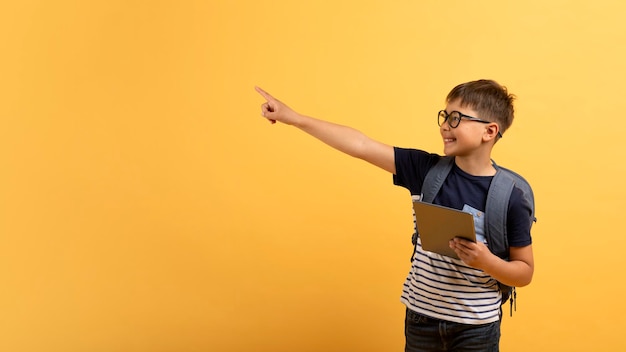 Positiver Schuljunge mit digitalem Tablet, der auf Kopierraum zeigt