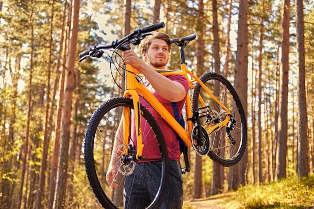 Positiver sportlicher Mann hält Mountainbike in einem Arm über seinem Kopf.