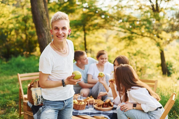 Positiver Typ mit Apfel, der vor Menschen steht Eine Gruppe junger Leute macht Urlaub im Freien im Wald Konzeption von Wochenende und Freundschaft