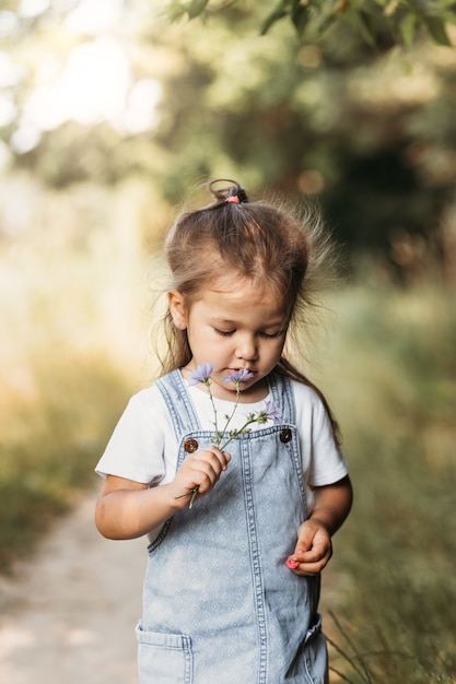 Positives charmantes kleines Mädchen, das sonnigen Sommertag genießt, Emotionen ausdrückt, Spaß hat, glückliches Kind, das am Sommertag spaziert