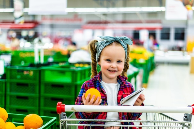 Positives kleines Mädchen, das Mandarinen im Laden kauft