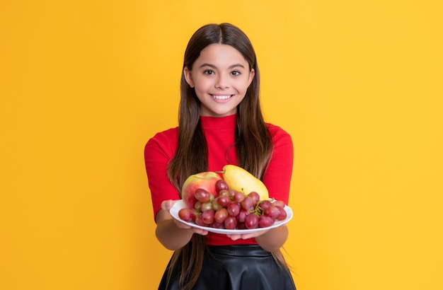 Positives Mädchen halten Teller mit frischen Früchten auf selektivem Fokus des gelben Hintergrundes