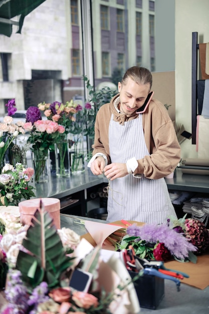 Positividad en el trabajo. Amable florista manteniendo una sonrisa en su rostro y mirando ikebana floral