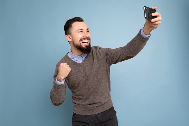 positivo bonito jovem moreno com barba por fazer e barba usando um suéter cinza casual