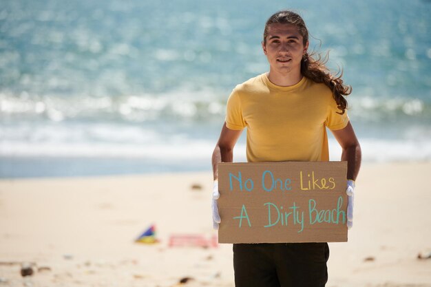 Positivo jovem ativista segurando ninguém gosta de um cartaz de praia suja