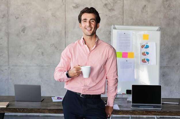 Positivo jovem empresário em pé ao lado da mesa bebendo café