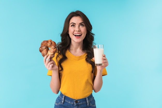 positivo lindo joven hermosa mujer posando aislada sobre pared azul con leche y pasteles.