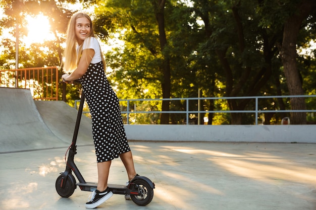 positivo optimista feliz adolescente en el parque caminando en scooter.