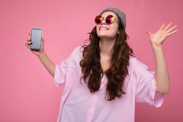 Positivo sonriente feliz atractiva joven morena mujer vistiendo elegante camisa rosa, sombrero gris y