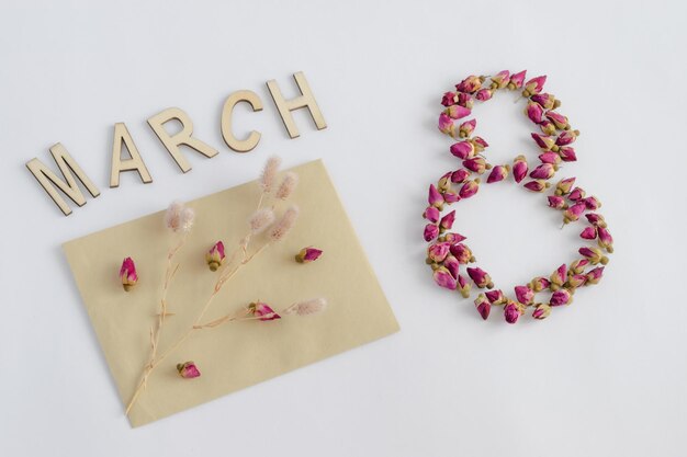 Postal para el 8 de marzo Día Internacional de la Mujer Número 8 forrado con capullos de rosas secas Sobre un fondo blanco un sobre con flores Foto