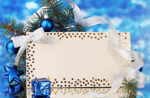 Postal en blanco, bolas de Navidad y abeto sobre fondo azul.