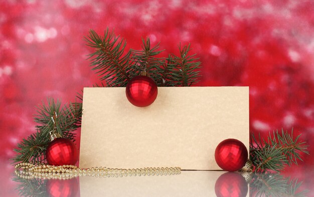 Postal en blanco, bolas de Navidad y abeto sobre fondo rojo.