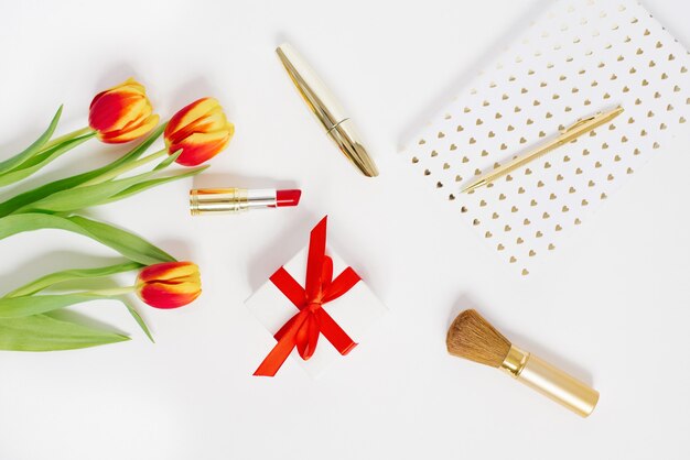 Postal de Dia dos Namorados, Dia das Mães ou 8 de março. Um buquê de tulipas, um presente com um laço vermelho, cosméticos e um caderno com uma caneta. Falt Lay blogger