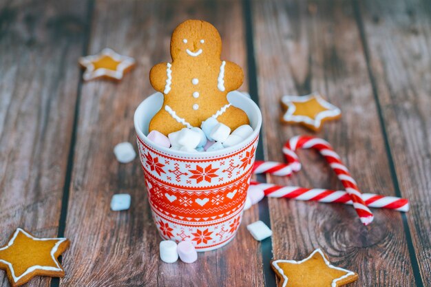 Postal de Natal com caneca vermelha do homem-biscoito com enfeites de natal na luz bokeh da árvore de Natal e doces listrados vermelhos de férias.