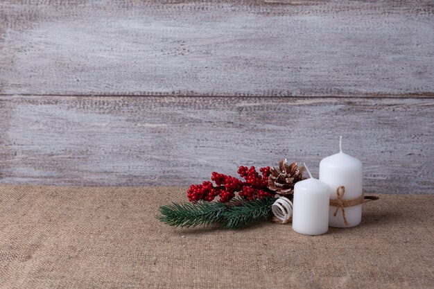 Postal de dos velas blancas y una rama de árbol de Navidad en una madera