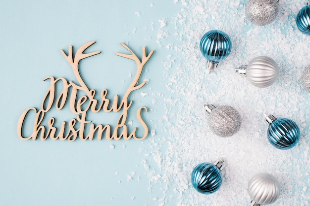 Postal de Navidad con concepto de deseos. Vista superior aérea de cerca la foto de adornos de árbol pequeño en la nieve y la Navidad felicidades inscripción volumétrica de madera sobre fondo de color pastel de escritorio de mesa