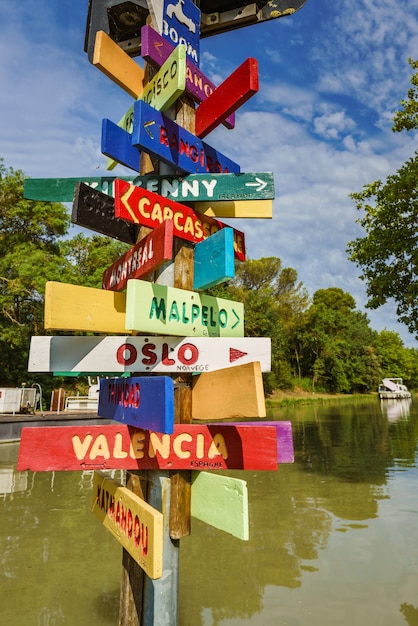 Poste com placas indicando a direção de várias cidades em cores vibrantes