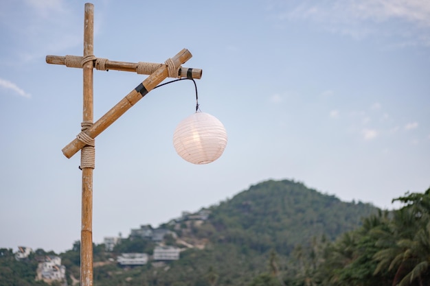 Poste de bambu e lâmpada branca com céu azul e montanha verde.