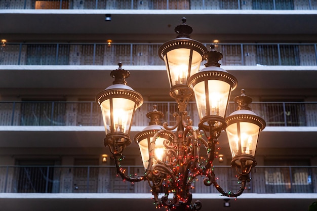 Poste de luz com cinco lâmpadas de estilo antigo acesas contra o pano de fundo de um edifício residencial alto