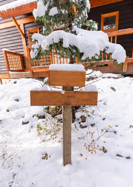 Poste de tabuleta de madeira com coberto de neve ou guia na frente da casa de madeira