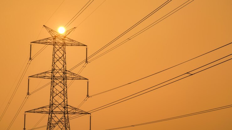 Poste de electricidad de alta potencia recortada contra el cielo naranja al atardecer Poste eléctrico en India