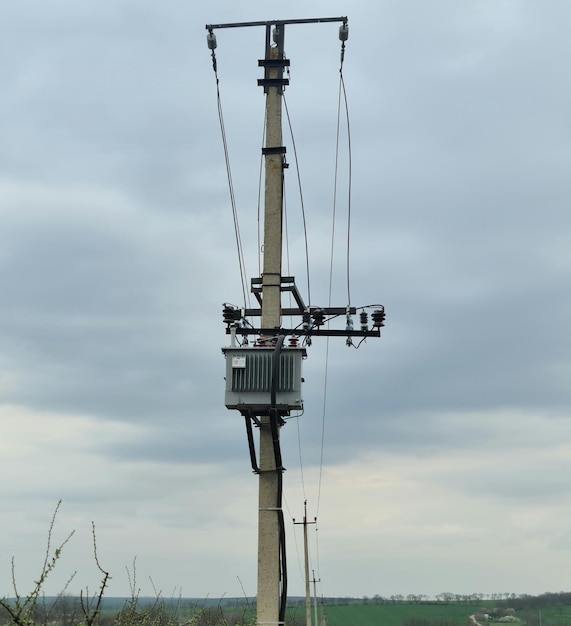 Un poste de energía con cables conectados y un cielo nublado en el fondo.