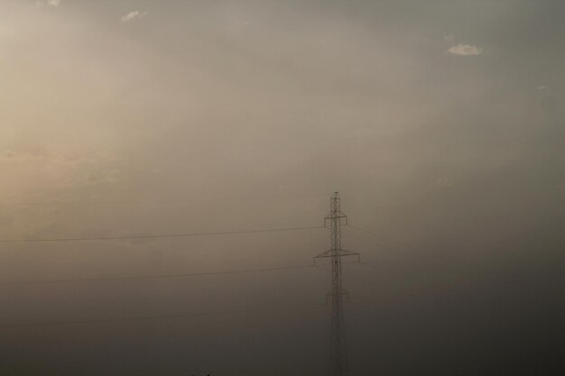 Un poste de energía está en la niebla y el sol brilla.