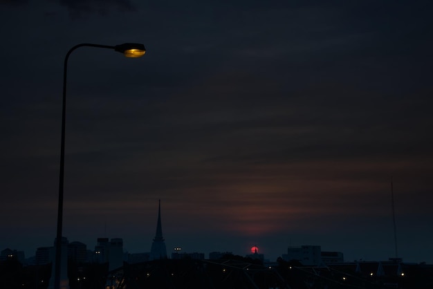 Un poste de luz halógena con pagoda budista y silueta de cruz de Cristo al atardecer