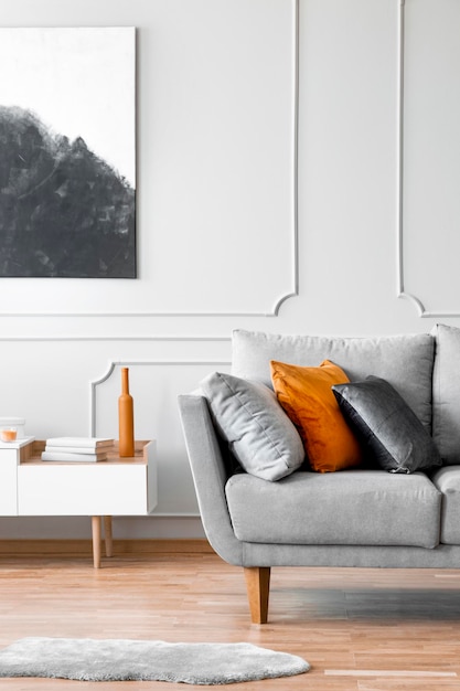 Poster über dem Schrank neben der Couch mit Kissen im grauen Wohnzimmerinterieur mit Fell Echtes Foto