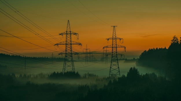 Postes de alta tensión en la niebla de la tarde en el atardecer de verano