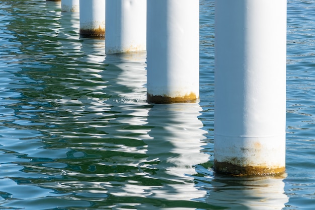 Postes de cais enferrujados na água do mar salgada. colunas brancas na diagonal. montagem de pilares para ponte. tempo ensolarado.