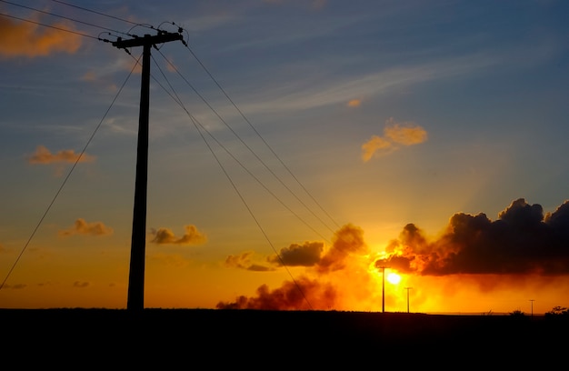 Postes electrizantes con fondo de cielo anaranjado al atardecer.