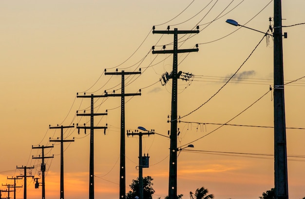 Postes electrizantes con fondo de cielo anaranjado al atardecer.