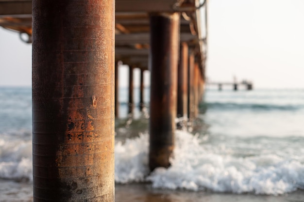 Postes de hierro muelle de madera olas salpicando alrededor de la playa