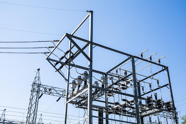 Postes y líneas eléctricas de acero en la estación de energía eléctrica de alta tensión contra el cielo azul claro