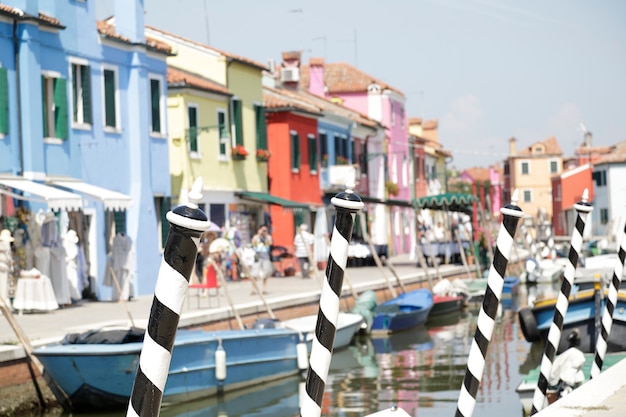 En los postes de primer plano pintados con rayas blancas y negras en el fondo (fuera de foco) las coloridas casas de la isla de Burano, Venecia, Italia.