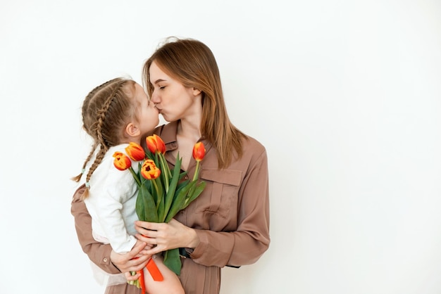 Postkarte für den 8. März Kleine Tochter küsst und umarmt Mutter mit gelben Blumen Tulpen Muttertag