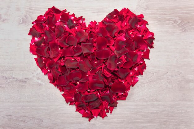 Postkarte mit einem großen Herzen aus roten Rosenblättern auf einem weißen Vintage-Holztisch