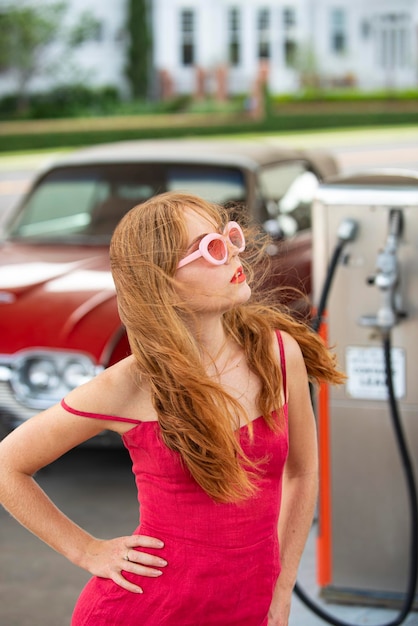 Posto de gasolina. uma linda mulher reabastecer o carro. senhora elegante contra automóvel retro vermelho.