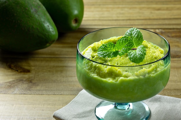 Postre de aguacate en tarro de cristal verde con menta encima sobre mesa de madera