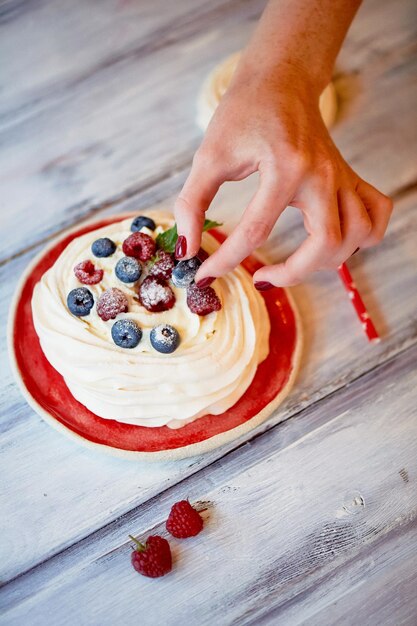 Postre Anna Pavlova con frambuesas y arándanos sobre superficie de madera blanca